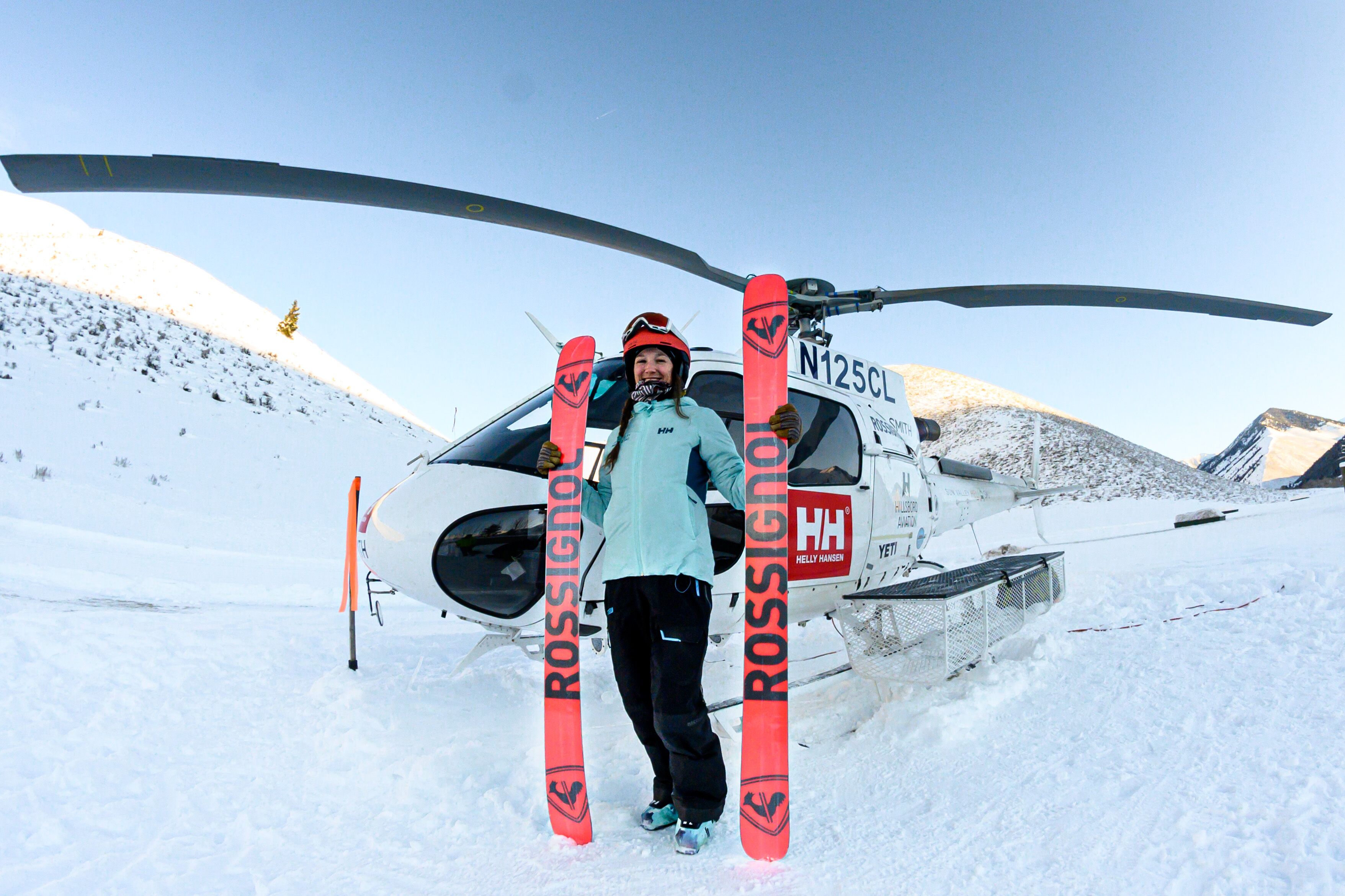 Una persona dempeus davant d'un helicòpter, amb els esquís als peus.