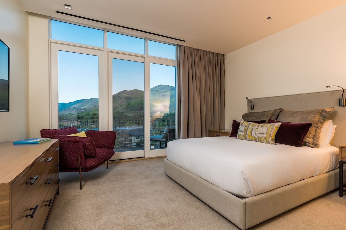Une chambre à coucher avec un grand lit, un bureau, une chaise et une vue sur l’extérieur.