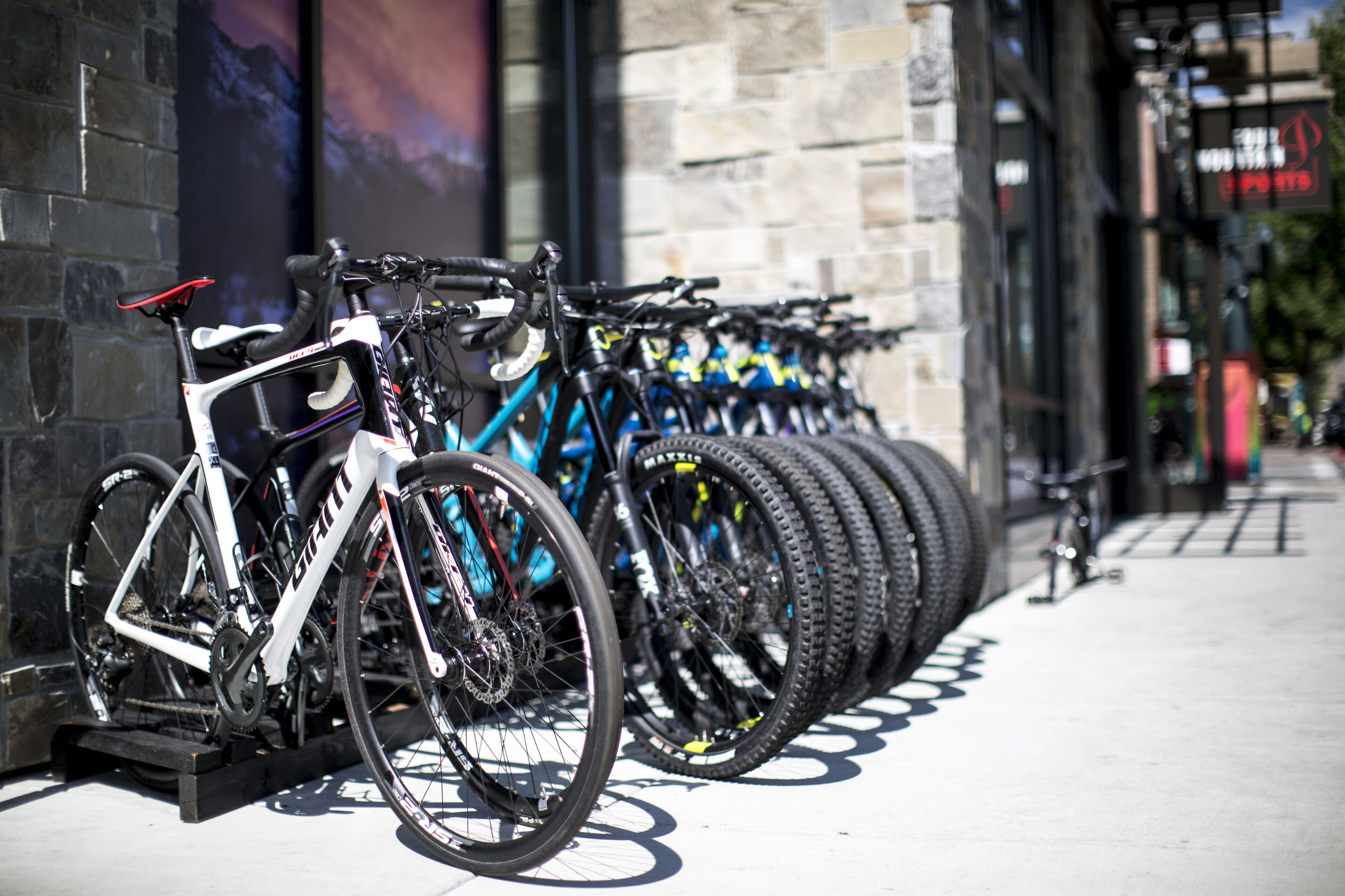 A row of bicycles parked against a brick wall, with a bike rack in front.