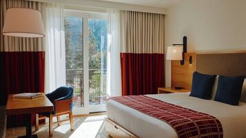 Habitación de hotel con cama, escritorio, silla, lámpara y vista al exterior.