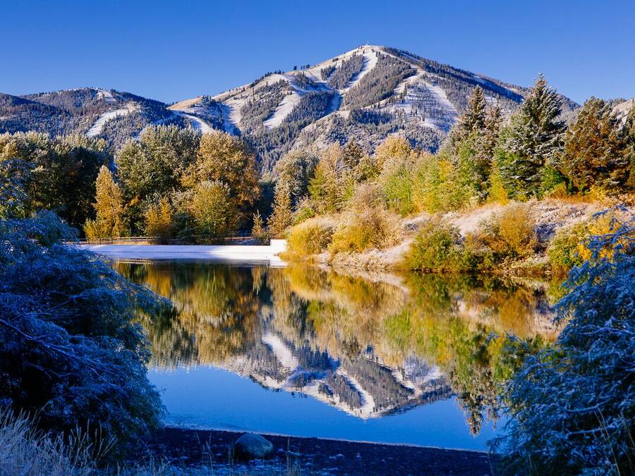 A serene lake with a mountain backdrop, surrounded by trees and shrubs.