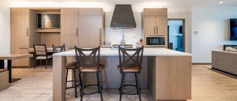 A modern kitchen with a central island, two bar stools, wooden cabinets, and a built-in microwave.