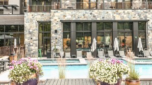 A hotel with a stone facade, outdoor pool with lounge chairs, and potted plants. - Limelight Hotel Ketchum (Ketchum)