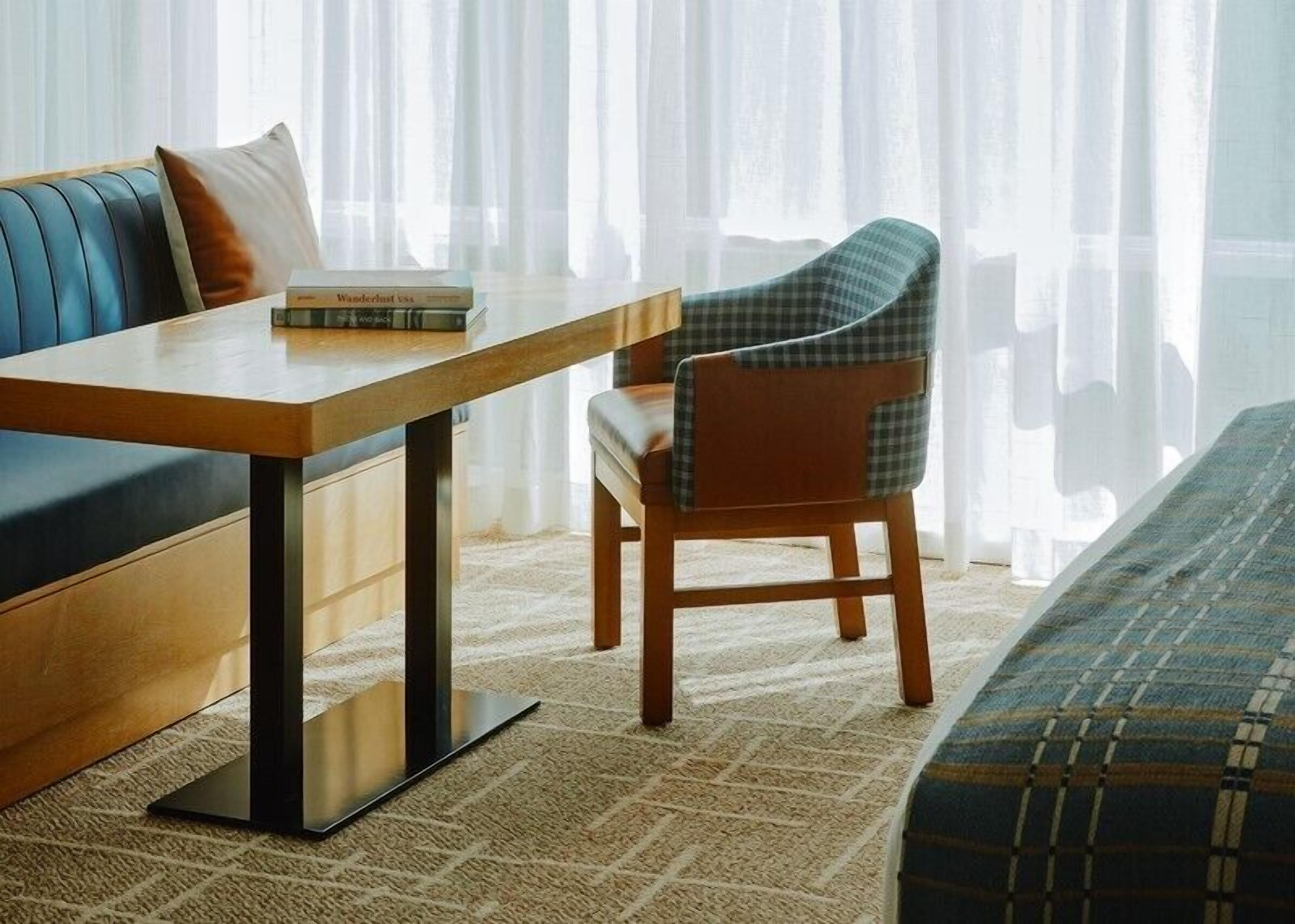 Ein modernes Hotelzimmer mit einer Couch, einem Holztisch und einem karierten Sessel.