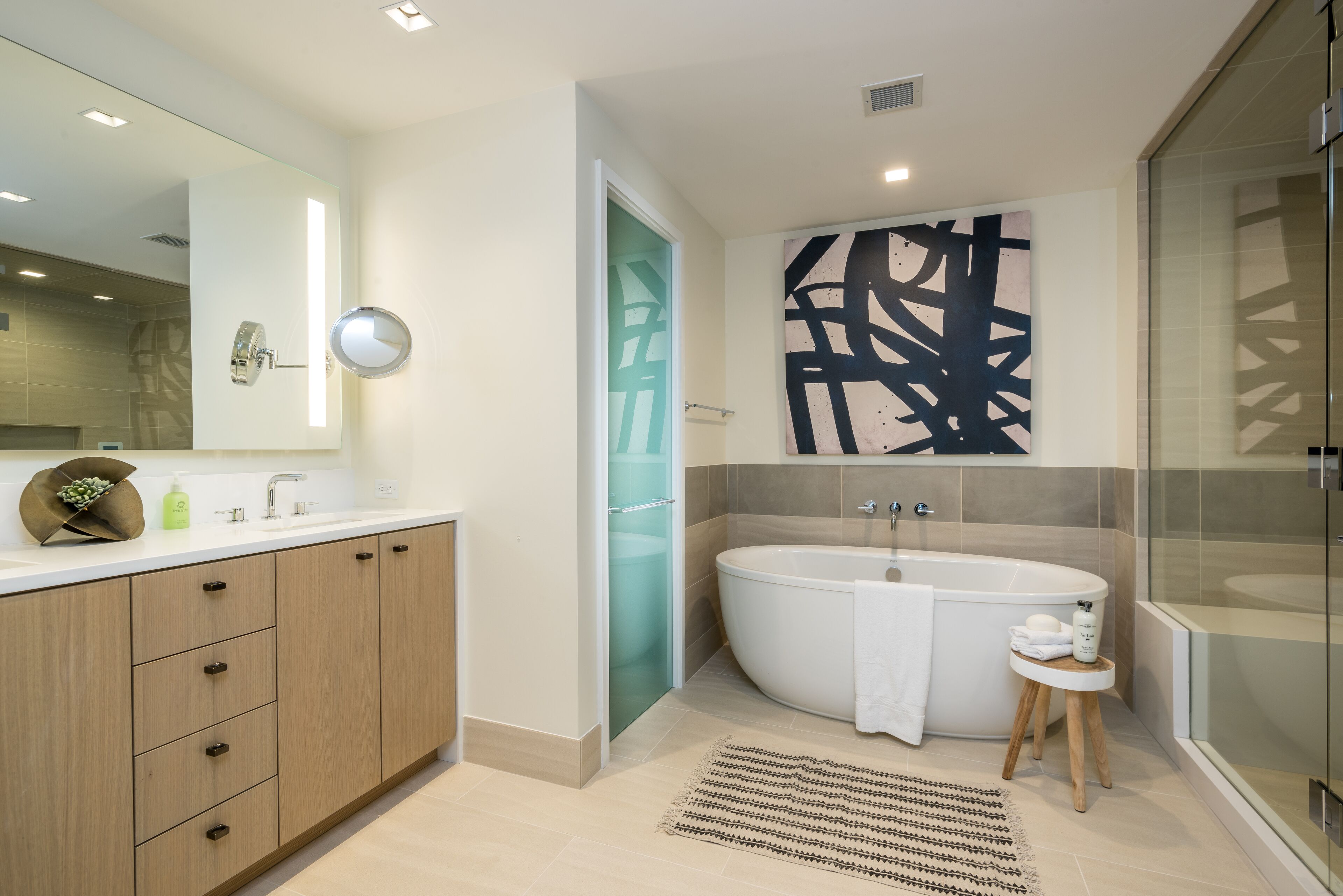 Un baño moderno con una bañera independiente, un espejo grande y una obra de arte abstracta contemporánea en la pared.