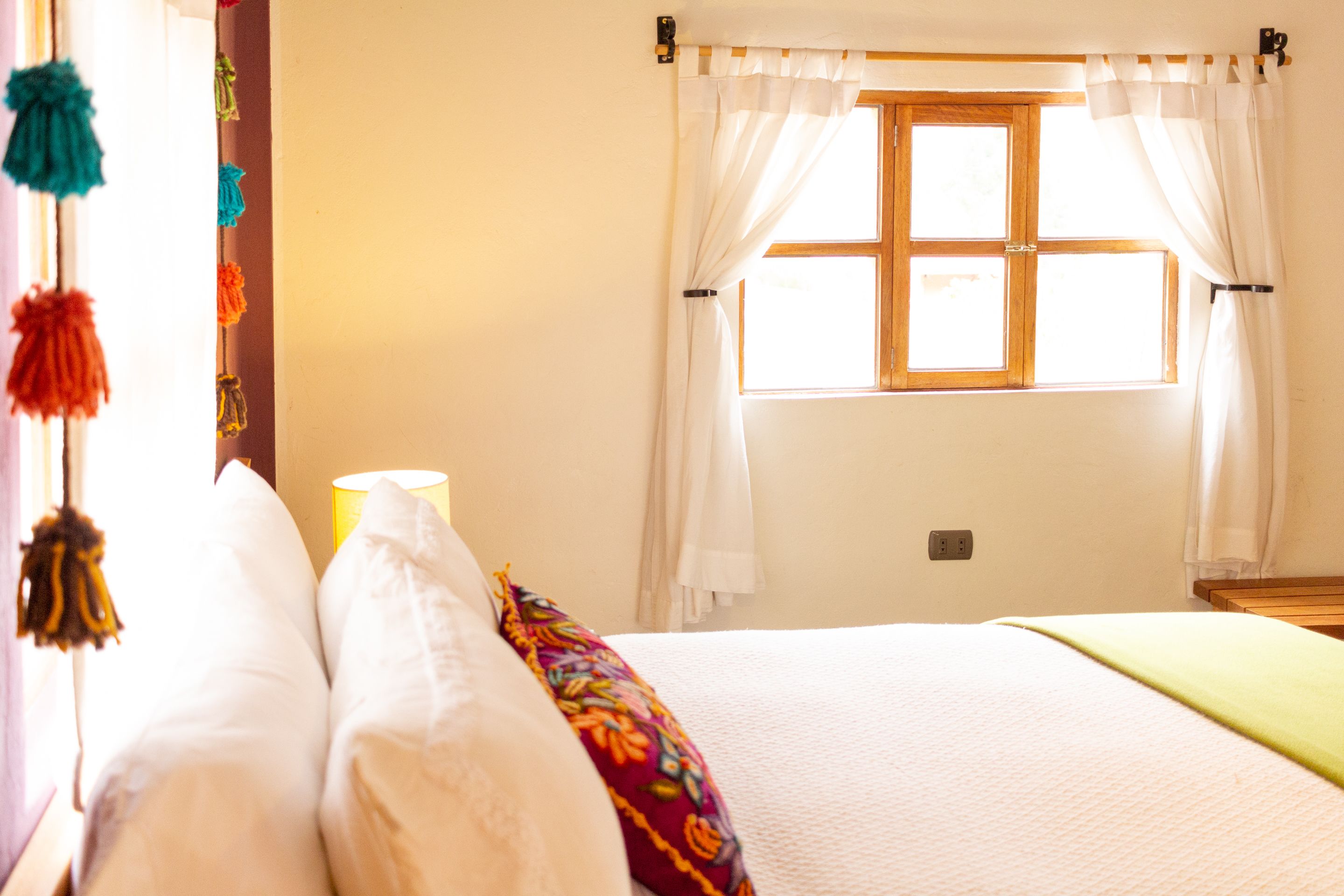 A bedroom with a bed, pillows, a window with curtains, and a wall socket.