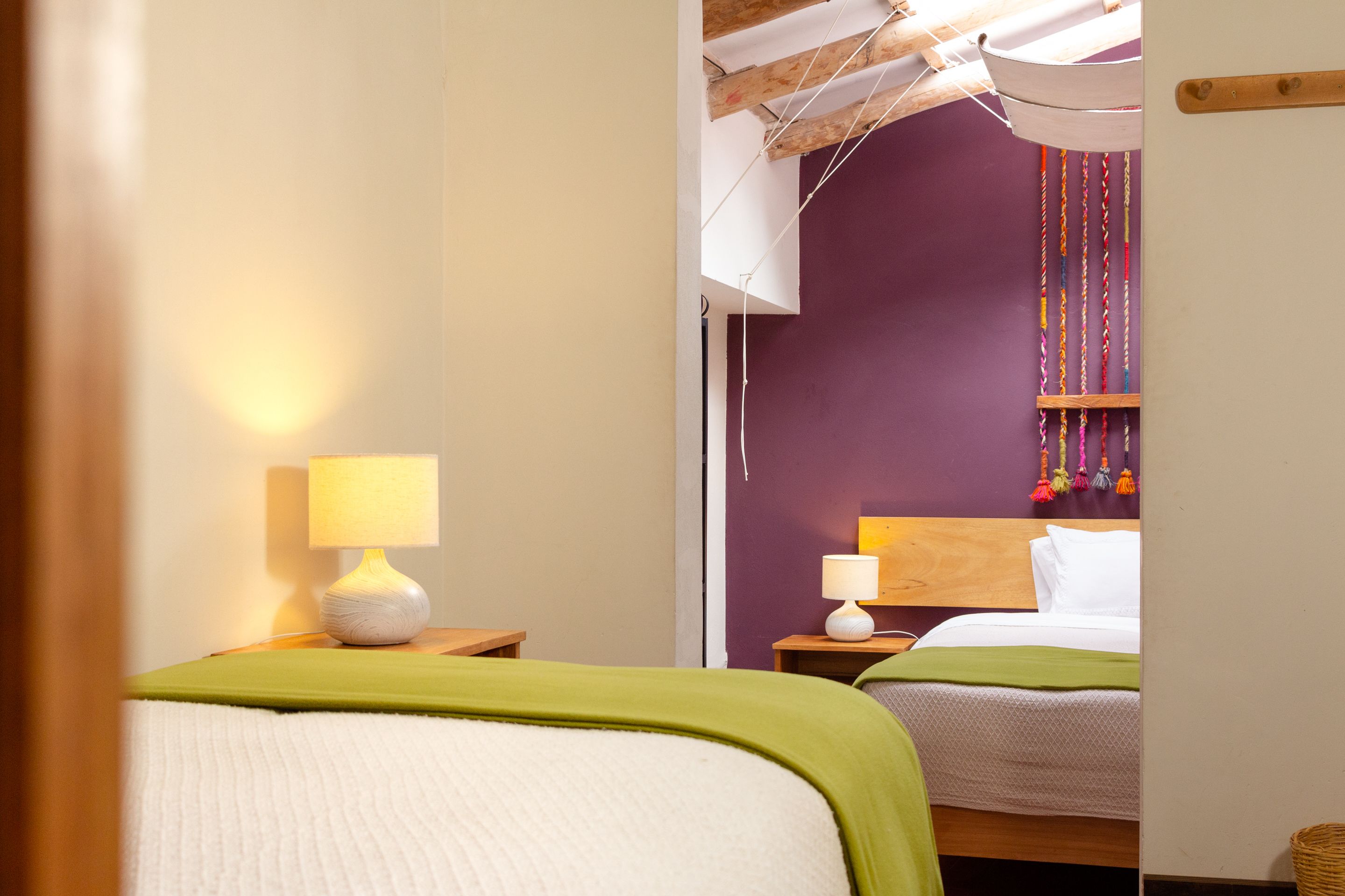 A hotel room with two beds, each with a green blanket, a wooden headboard, and a white pillow. There are two bedside tables with lamps.