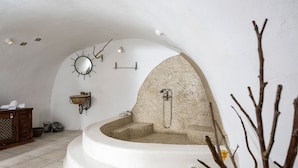 Ein Wellnessbereich mit einer gebogenen Badewanne, einem Holzschrank, einem Spiegel und einer Steinwand.