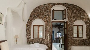 Ein Schlafzimmer mit Steinwand, einem Bett mit weißer Bettwäsche und einem Fenster mit Holzrahmen.