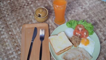 A meal consisting of toast, eggs, and vegetables on a plate, accompanied by a glass of orange juice and a small container of sauce, all placed on a woven tablecloth.