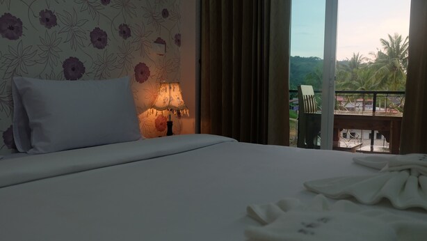A hotel room with a bed, a nightstand with a lamp, a view of the outdoors through a balcony, and a patterned wall. - PhuTubkaek View House (Krabi)
