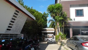 A parking area with motorcycles and a car, surrounded by buildings and palm trees. - PhuTubkaek View House (Krabi)