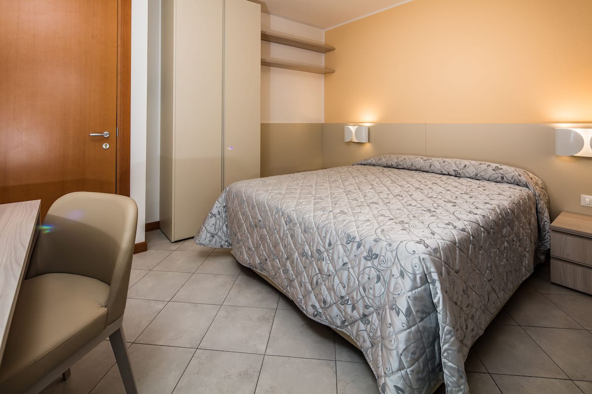 Una camera da letto con un letto, comodini, una sedia e una porta.