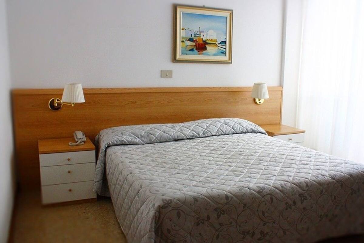 Una camera da letto con una testiera in legno, un letto con copriletto trapuntato, due comodini con lampade e un quadro appeso al muro.