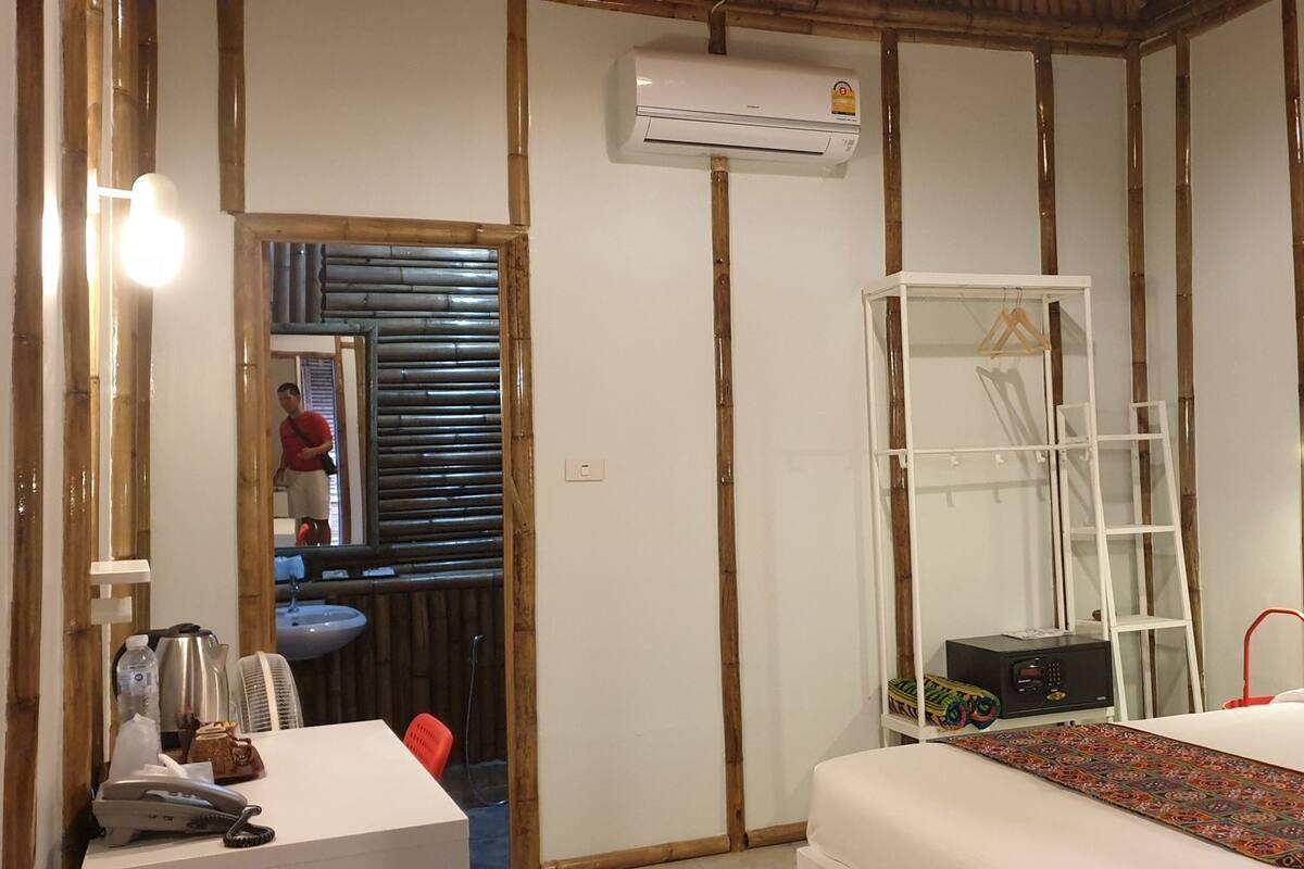 A room with a bed, a desk with a telephone, a sink, and an air conditioning unit.