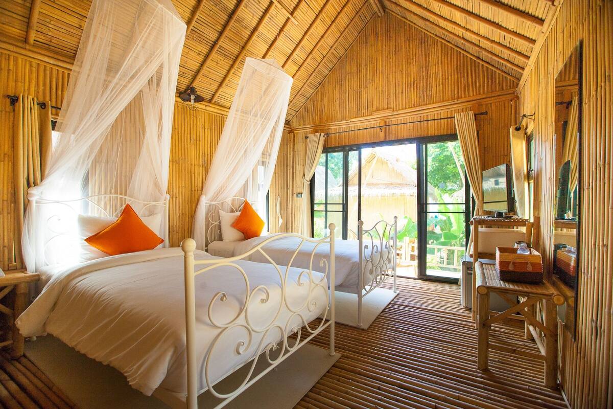A room with a bed, a desk, and a window with a view of greenery.