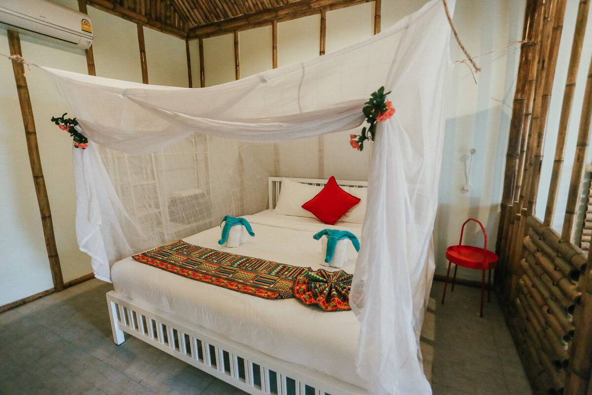 A bed with a canopy, a red pillow, and a colorful blanket.