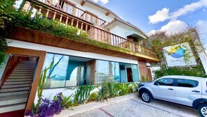 A two-story building with a balcony, a car parked in front, and a sign with a logo. - Sol Nascente Praia Hotel (Natal)