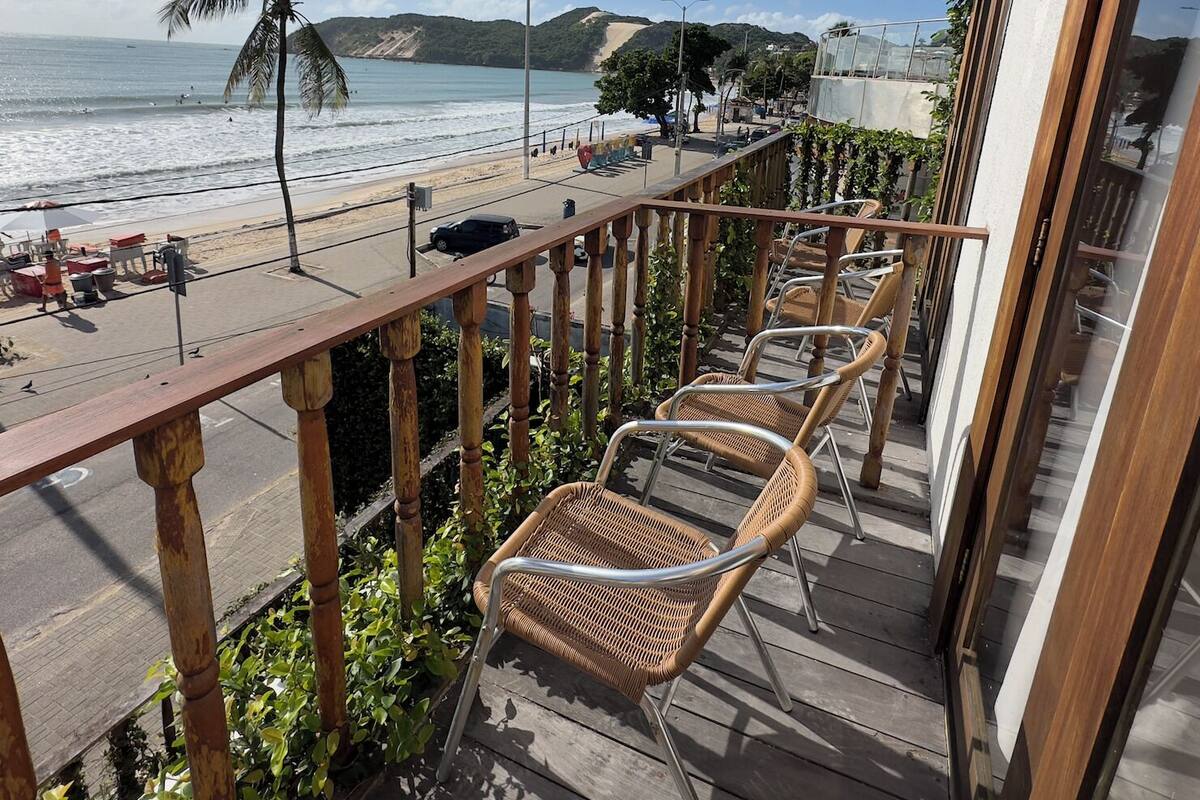 Un balcon avec des fauteuils en osier donnant sur une plage et l’océan.