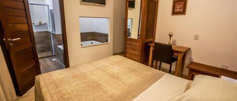 Un dormitorio con una cama, un armario de madera, un escritorio con una silla, un espejo y una ventana pequeña.