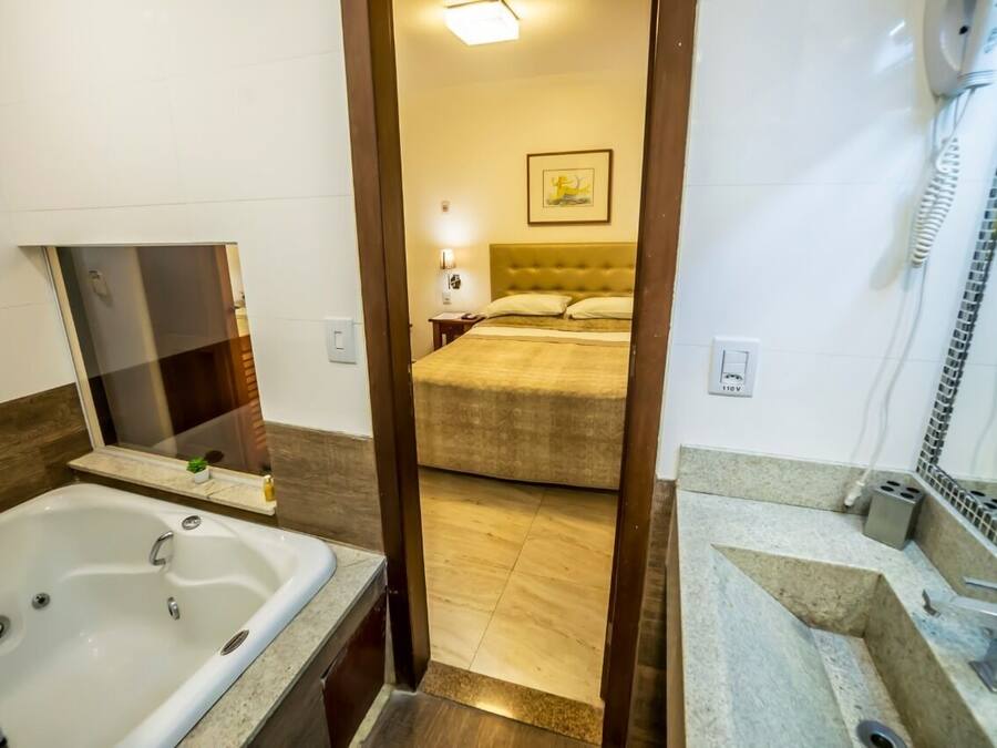 A hotel room with a large bathtub, a bed with a headboard, a bedside table, and a wall-mounted phone.