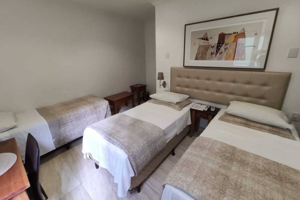 A hotel room with three single beds, a small desk, and a chair.