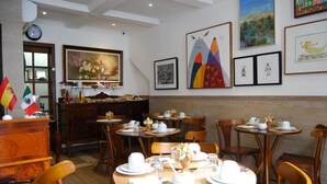 Un comedor con mesas redondas preparadas para el desayuno, sillas de madera y un mostrador de buffet con alimentos.