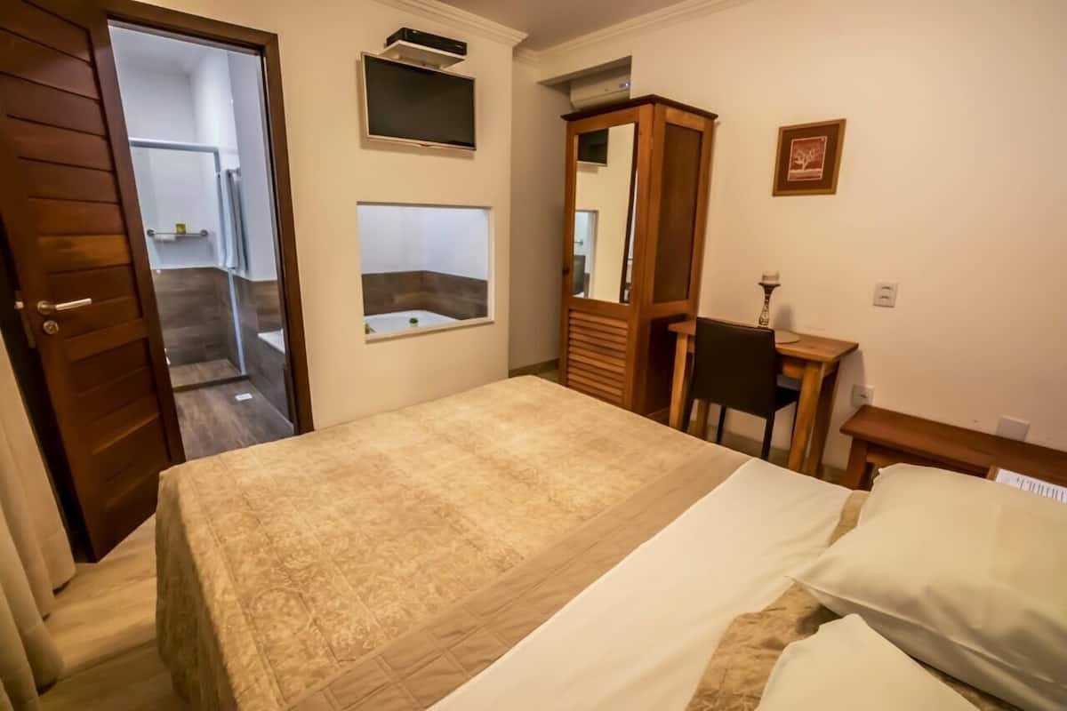 A bedroom with a bed, a wooden wardrobe, a desk, a chair, and a mirror.