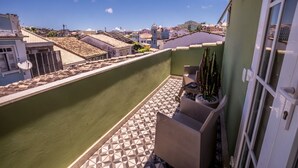 Un balcón con suelo de baldosas geométricas, una planta en maceta y vista a la ciudad.