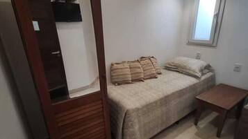 A bedroom with a bed, a wooden wardrobe, a small table, and a window.