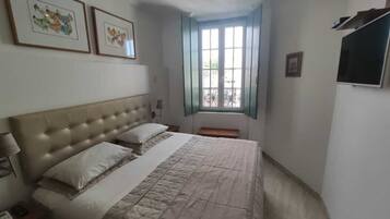 Un dormitorio con una cama grande, una mesita de noche, un ventanal con vistas y cuadros enmarcados en la pared.