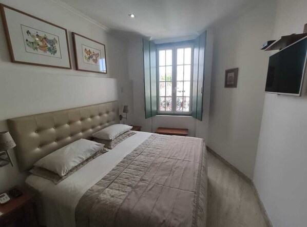 A bedroom with a large bed, a nightstand, a window with a view, and framed pictures on the wall.