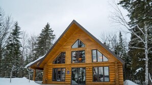 Una cabaña de troncos con techo triangular, ventanas amplias y un paisaje cubierto de nieve.