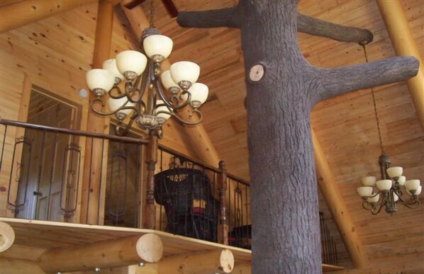 Interior de madeira com um candelabro, uma escada e um tronco de árvore.