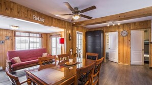 A wooden interior with a dining table, chairs, a red sofa, and a ceiling fan.