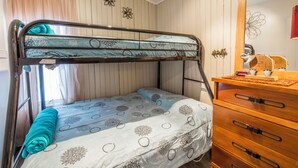 A bunk bed with a blue and white patterned bedspread, a wooden dresser with drawers, and a mirror above the dresser.