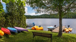 A lakeside setting with a dock, a boat, and colorful kayaks. - Le Bois Rond Des Ruisseaux (Saint-Tite-des-Caps)
