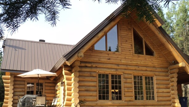 A log cabin with a dining area, large windows, and a metal roof. - Le Bois Rond Des Ruisseaux (Saint-Tite-des-Caps)