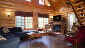 A log cabin interior with a sofa, armchair, and a fireplace. - Le Bois Rond Des Ruisseaux (Saint-Tite-des-Caps)
