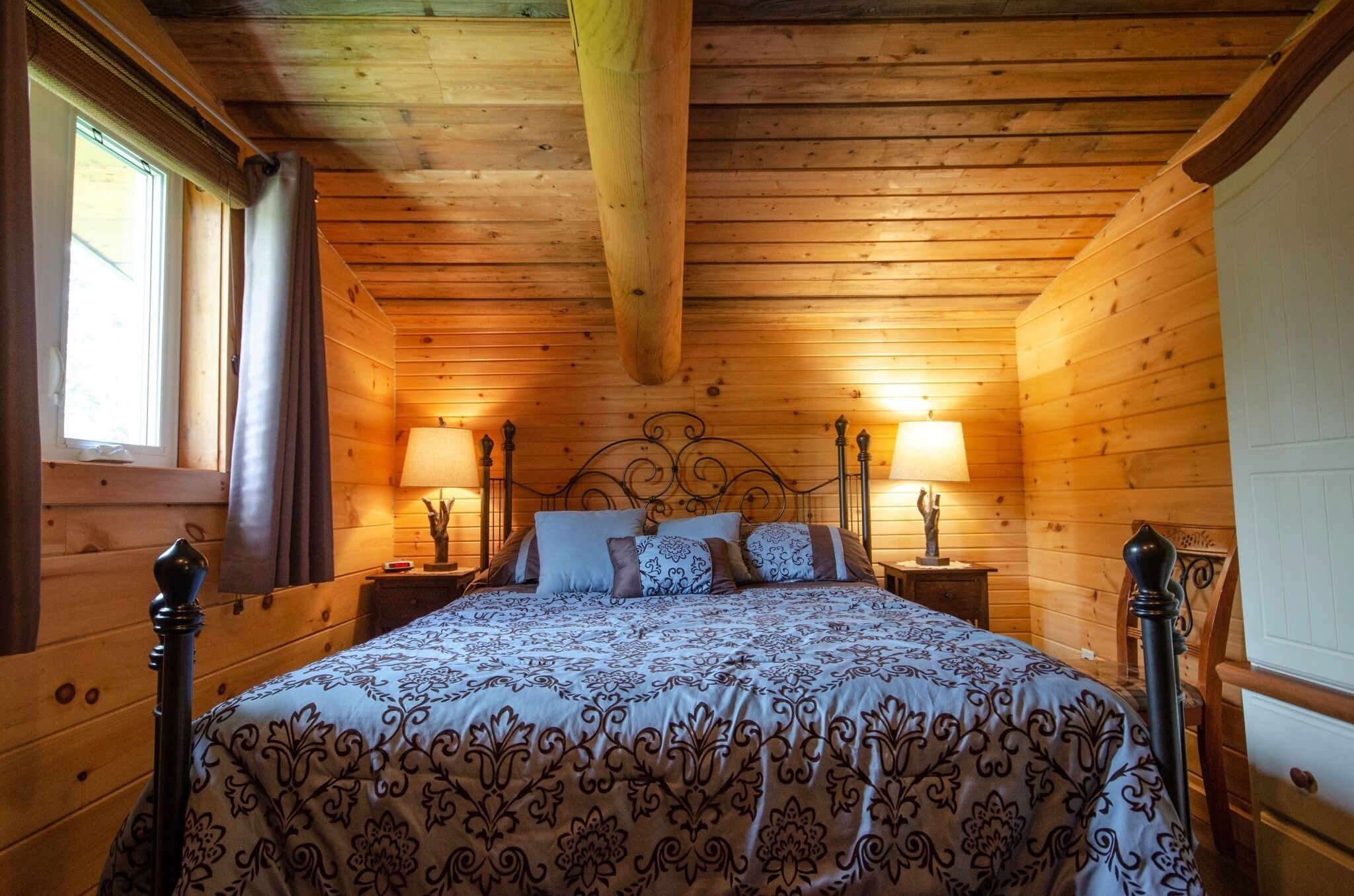 A wooden cabin bedroom with a bed, two nightstands, and two wall-mounted lamps.