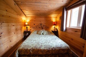 Une chambre dans une cabane en bois, avec un lit, deux tables de chevet et une fen être.