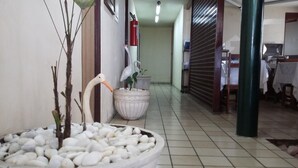 A hallway with a potted plant, a white swan statue, and a fire extinguisher on the wall. - Escuna Praia Hotel (João Pessoa)