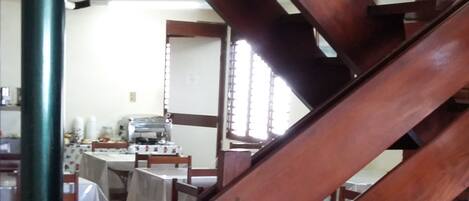 A wooden staircase with a green pillar, leading to a dining area with tables and chairs.