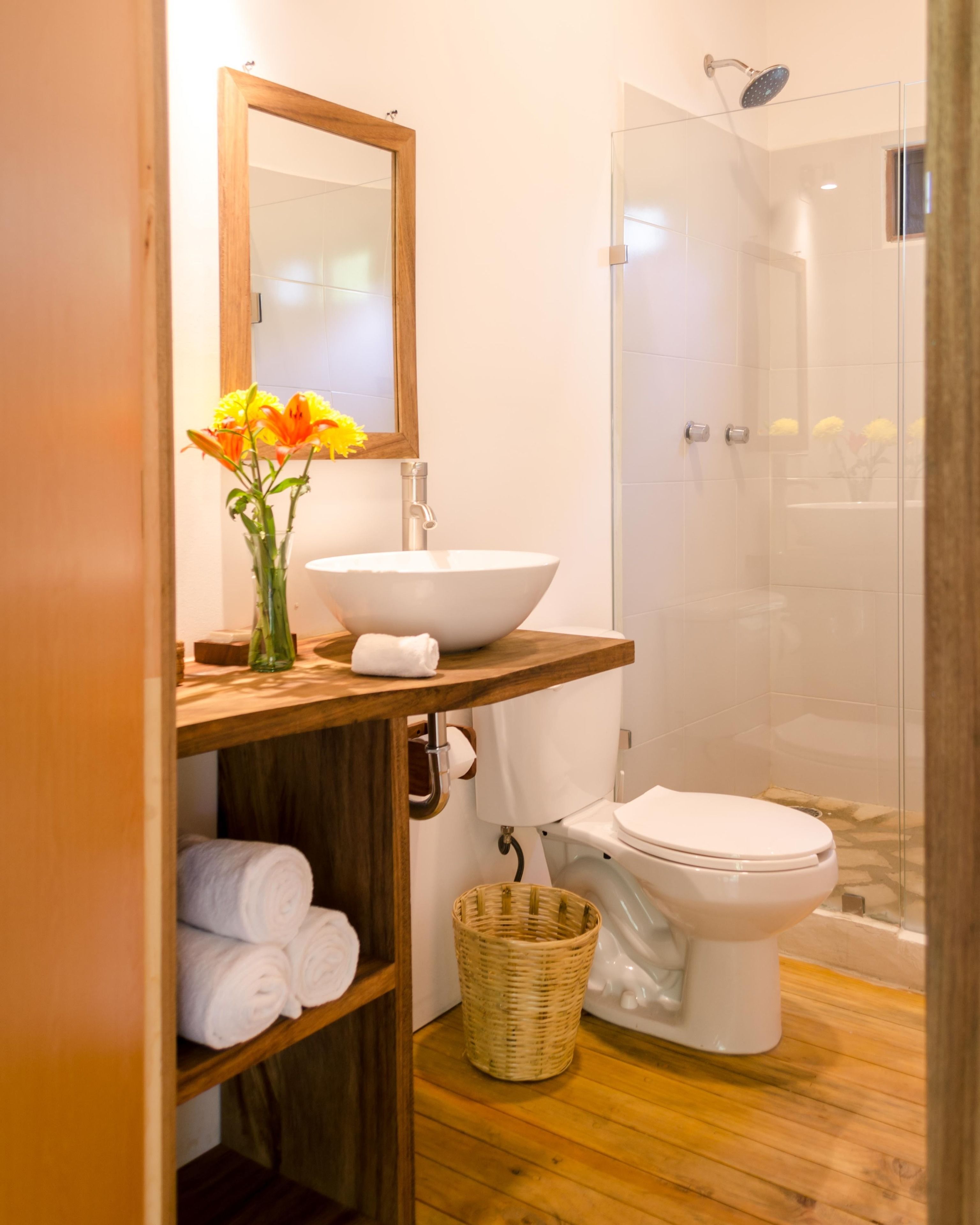 Une salle de bain avec un meuble-lavabo en bois, un lavabo blanc, un miroir, des toilettes et une douche à parois de verre.
