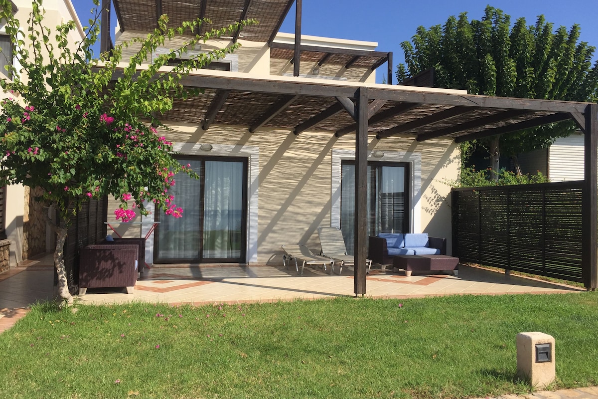 Uma casa moderna com varanda coberta, porta de vidro e área de estar com sofá e poltronas.