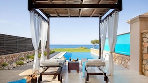 A covered outdoor area with a pool, two lounge chairs, and a view of the ocean. - Al Mare Villas (Rhodes)