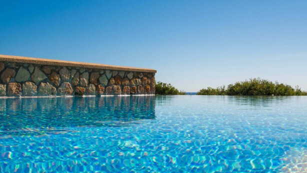 A clear blue pool with a stone wall and a view of a distant island. - Al Mare Villas (Rhodes)