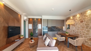 A modern living room with a sofa, TV, and dining area with chairs. - Al Mare Villas (Rhodes)