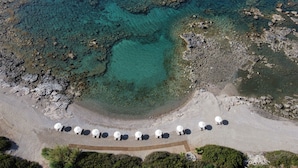 An aerial view of a beach with clear turquoise water, rocky shorelines, and a row of white umbrellas along the shore. - Al Mare Villas (Rhodes)