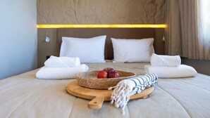 A neatly made bed with white pillows, a woven basket with apples, and a wooden cutting board with a towel and a striped cloth. - Al Mare Villas (Rhodes)